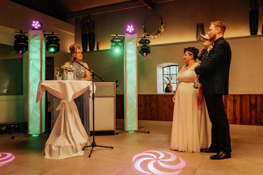 Rednerin am Stehtisch mit Mikrofon, daneben das Brautpaar mit Sohn auf dem Arm