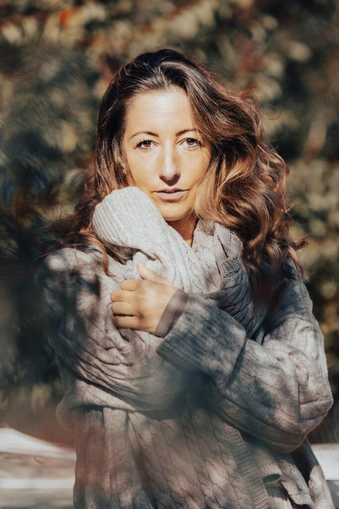 Portrait einer Frau mit langen welligen Haaren im grauen Strickpullover, warmes Herbstlicht